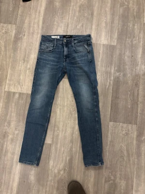 Replay anbass  - Säljer ett par snygga jeans från Replay i modellen anbass då de tyvärr inte passar mig längre. Jeans i blå tvätt med snygga slitningar som ger en modern look. De är använda men fortfarande i fint skick utan några skador. Storlek W29 L30