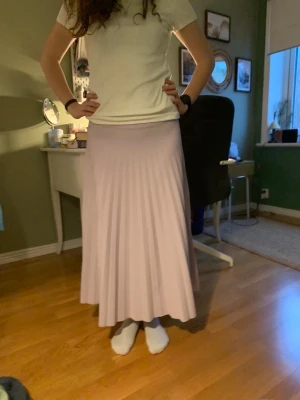 Ljuslila plisserad maxikjol - Säljer en lång, ljuslila plisserad maxikjol med mjukt fall. Kjolen har en bred midjeresår och är tillverkad i ett tunt, följsamt material som ger ett snyggt flow. Perfekt för dig som gillar en feminin och enkel stil.