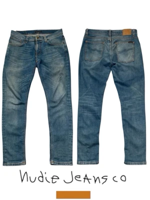 Blå jeans från Nudie Jeans Co - Snygga blå jeans från Nudie Jeans Co med klassisk femficksmodell och raka ben. Jeansen har en ljus tvätt med slitningar och kontrastsömmar samt en brun patch med orange logga bak i midjan. Tillverkade i bomull för en bekväm känsla.