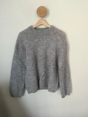 Grå stickad ulltröja med vida ärmar från Kappahl - Mysig grå stickad tröja med rund hals och avslappnad passform. Tröjan har långa ärmar och ribbade muddar vid hals, ärmslut och nederkant. Tröjan är endast använd en gång och är i mycket fint skick! Tröjan är i storlek S men skulle säga att den även passar M! Hör gärna av dig vid frågor och funderingar! 