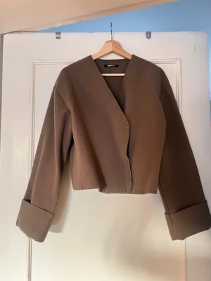 Gina tricot jacka - 🤎 Brown wrap-style jacket 🤎   Minimalist brown jacket with a clean wrap-style front and no visible buttons. Features wide cuffs, long sleeves, and subtle stitched edge details for a modern touch. The structured yet soft fabric makes it perfect for both casual and dressed-up looks.    • Color: Brown   • Style: Wrap / open front   • Sleeves: Long with wide cuffs   • Detail: Decorative stitched edges   • Fit: Relaxed yet structured   • Condition: Very good condition    #brownjacket #minimalstyle #n