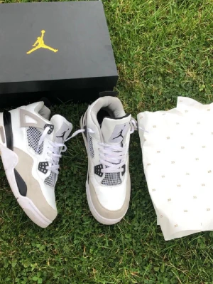 Air Jordan 4 Retro White - Snygga Air Jordan 4 Retro sneakers i vitt och grått med svarta detaljer. Ovandel i läder och mocka, meshpaneler på sidorna och klassisk Jumpman-logga på plösen. Skorna har högt skaft och vita skosnören. Perfekta för dig som gillar streetwear och basketstil. Priset går att pratas om vid snabb affär