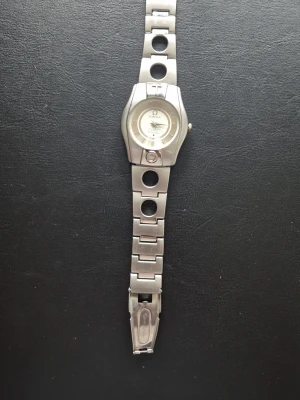 Silver klocka - Stilren Omega Constellation klocka i silverfärgat metallarmband med unika cirkelformade länkar. Urtavlan är ljus med romerska siffror och klassisk Omega-logga. Perfekt accessoar för dig som gillar exklusiv och tidlös design. Har man frågor så kan man gärna ställa.