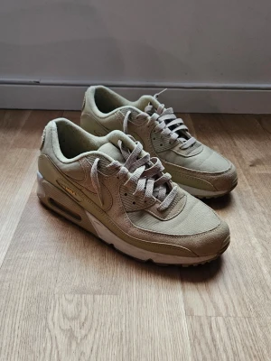 Beige Nike Air Max 90 sneakers - Snygga beige Nike Air Max 90 sneakers. Skorna har ovandel i mesh och mocka, med synlig Air-enhet i sulan och diskreta gula detaljer på plös och häl. 