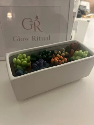 Dekorativ ljuslåda med suckulenter - Unik rektangulär ljuslåda från Glow Ritual med färgglada vaxfigurer formade som små suckulenter. Ljusen är placerade i en vit keramikkruka och har detaljer i grönt, lila och orange. Perfekt som dekoration för att skapa mysig stämning.
