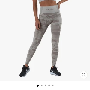 Beige camo leggings från Gavelo - Snygga beigea leggings från Gavelo med hög midja och camouflagemönster. De har ribbade detaljer över låren och är tillverkade i ett stretchigt material som sitter tight. Perfekta för träning eller en sportig look. Strotlek S och använda 1 gång