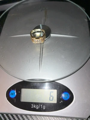 Guldfärgad ring med stenar 14 karat  - Snygg 14 karat guld  ring med rektangulär form och infattade klara stenar framtill. Ringen har en bred design och glänsande finish som ger ett lyxigt intryck. Perfekt accessoar för att lyfta din stil.