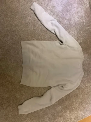 Vitt stickad tröja - En enkel och stilren ljusgrå stickad tröja med rund hals och långa ärmar. Tröjan har ribbade muddar vid ärmslut och nederkant. Perfekt att matcha med jeans eller kjol. Materialet känns mjukt och bekvämt.