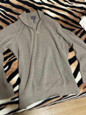 Beige stickad halvzip-tröja - Snygg beige stickad tröja med halvzip och hög krage. Tröjan har ribbad struktur och långa ärmar, perfekt för lager på lager. Passar till både jeans och chinos för en avslappnad stil.