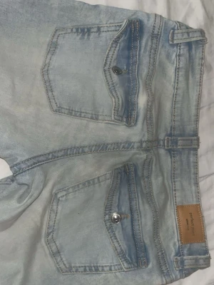 Ljusblå bootcut jeans från Perfect Jeans - Säljer ett par ljusblå bootcut jeans från Perfect Jeans med snygga ficklock och silverfärgade knappar bak. Jeansen har låg midja och utsvängda ben, perfekt för en trendig look. Klassisk denim med cool tvätt och detaljer.