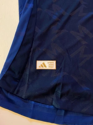 Manchester United blå matchtröja Adidas - Säljer en blå Manchester United matchtröja från Adidas med Snapdragon-logga på bröstet. Tröjan har ett subtilt mönster i tyget och klubbmärket på vänster sida. Tillverkad i lätt och ventilerande material, perfekt för fotbollsträning eller match.