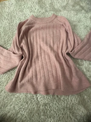 Rosa stickad tröja från 157 - Mysig stickad tröja i ljusrosa från 157 med ribbade muddar och rund hals. Tröjan har ett rakt, avslappnat snitt och vertikala stickade ränder som ger en snygg struktur. Perfekt för lager-på-lager och chill dagar.