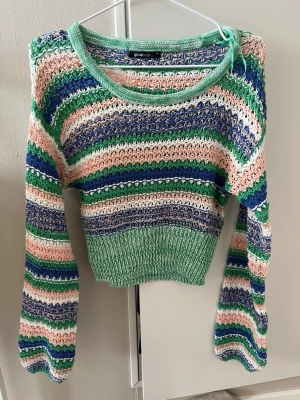 Färgglad stickad tröja från Gina Tricot - Säljer en stickad tröja från Gina Tricot med breda ränder i grönt, blått, vitt och ljusrosa. Tröjan har rund halsringning, långa ärmar och ribbstickad nederkant. Materialet är grovstickat och ger en luftig känsla. Perfekt för dig som gillar färg och mönster.