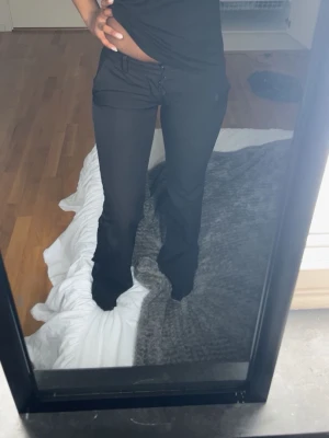 Svarta BikBok kostymbyxor  - Snygga svarta kostymbyxor med bootcut-modell med slit där nere och låg midja. Byxorna har bälteshällor och knappstängning framtill. Perfekta för en clean och stilren look. Materialet ser ut att vara en mjuk och stretchig blandning, vilket ger skön passform.