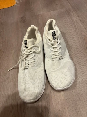 Vita sneakers från Your Turn - Snygga helvita sneakers från Your Turn med klassisk låg profil. Skorna har ovandel i meshmaterial för bra andningsförmåga och vita snören. Perfekta för en clean och stilren look till vardagsoutfiten.