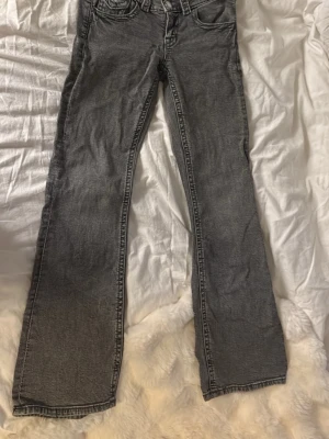Grå jeans från Gina Tricot - Säljer ett par grå jeans från Gina Tricot i storlek 152. Jeansen har raka ben, dubbla silverknappar i midjan och klassisk femficksmodell. Materialet är denim med en tvättad look som ger en cool vibe.