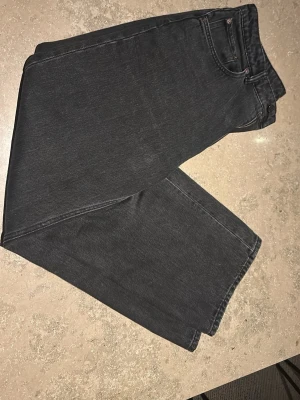 Svarta raka jeans med hög midja - Säljer ett par svarta jeans med rak passform och hög midja. Jeansen har klassisk femficksdesign och bälteshällor. Materialet är denim i bomull och de har en stilren look utan slitningar eller dekorationer.