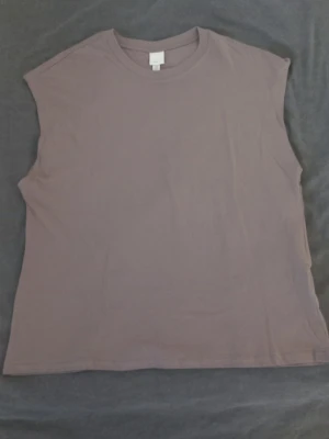Grå ärmlös topp från H&M Basics HELT NY - En enkel och stilren grå ärmlös topp från H&M Basics. Toppen har rund halsringning och är tillverkad i mjuk bomull, perfekt för en avslappnad look. Passar bra till jeans eller shorts för en clean och enkel stil.