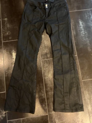 Svarta coated jeans bootcut - Säljer ett par svarta coated jeans från Nelly i storlek 38/short. De är använda 1-2 gånger men är lite för små för mig. Passar ca 165 cm. Inga tecken på användning💗💗