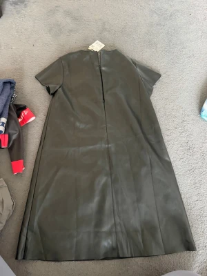 Svart klänning i skinnimitation från Mango - Cool svart klänning i skinnimitation från Mango med korta ärmar och rak passform. Klänningen har dragkedja bak och en minimalistisk look som passar perfekt till sneakers eller boots.