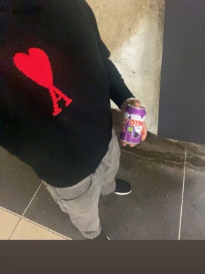 Svart stickad tröja med röd hjärt-A - Cool svart stickad tröja från AMI Paris med ett stort rött hjärta och bokstaven A på bröstet. Tröjan har en klassisk rund hals och långa ärmar. Perfekt för dig som vill ha en statement piece i garderoben.