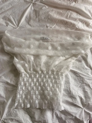 Vit prickig off shoulder topp - Trendig vit off shoulder topp från Designbysi med stora prickar i mesh-tyg. Toppen har smockad midja som ger en snygg siluett. Perfekt för dig som vill sticka ut med en unik och luftig look. Storleken är i xs/s och är använd endast en gång! 💕Pris går att diskuteras :)