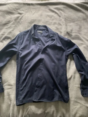 Mörkblå skjorta från Selected Homme - Stilren mörkblå skjorta från Selected Homme med klassisk krage och långa ärmar. Skjortan har knappar framtill och är tillverkad i ett mjukt bomullsmaterial. Perfekt för en clean och enkel look.