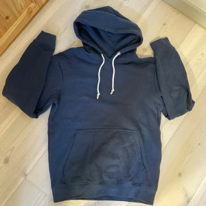 HOODIE | PIER ONE. - Snygg mörkblå hoodie med stor känguruficka framtill och vit dragsko i huvan. Klassisk modell med ribbade muddar vid ärmslut och nederkant. Perfekt för en avslappnad och cool stil.
