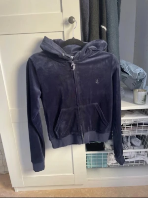 Mörkblå velourhoodie Juicy Couture - Säljer en mörkblå velourhoodie från Juicy Couture i storlek S. Hoodien har dragkedja, två fickor fram och en broderad JC-logga på bröstet. Klassisk juicy-stil med mjukt material och ribbade muddar vid ärmar och nederkant. Perfekt för en chill och trendig look.