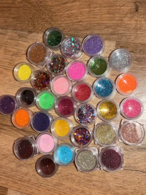 Stort set med nagelglitter i burkar - Säljer nagelglitter i små burkar. Flera olika färger som rosa, blå, guld, silver, grön, lila och orange samt olika former på glitter, både fina och chunky flakes. Perfekt för kreativa nageldesigner och nail art. Materialet är plast och glitter. 5 kr styck! Hela setet (33 burkar) 160kr