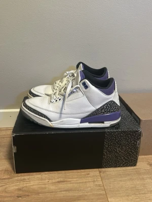Air Jordan 3 Retro vit/lila - Säljer ett par Air Jordan 3 Retro sneakers i vitt läder med lila och svarta detaljer samt klassiskt elephant print runt hälen och tån. Skorna har vita skosnören, svart innersula och Jumpman-logga på plösen. Perfekta för dig som gillar ikoniska sneakers.