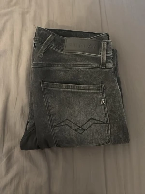 Replay svarta tvättade jeans - Säljer ett par svarta tvättade jeans från Replay med klassisk femficksmodell och snygga detaljer på bakfickan. Jeansen har en rak passform och är tillverkade i ett mjukt denimtyg som ger en skön känsla. Perfekta för dig som gillar en avslappnad men stilren look.