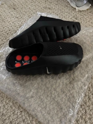 Svarta Nike mind tofflor - Säljer ett par svarta Nike tofflor med perforerad ovandel och vågig sula. Insidan har en cool design. 