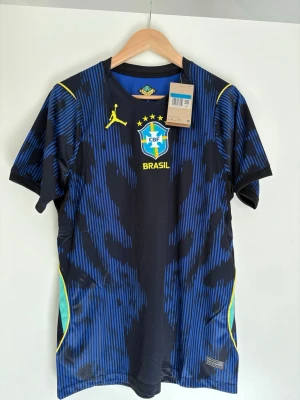 Brasilien matchtröja blå Nike - Snygg blå och svart Brasilien matchtröja från Nike med gula detaljer och CBF-logga på bröstet. Tillverkad i lätt och ventilerande material, perfekt för fotboll eller träning. Korta ärmar och modern passform.