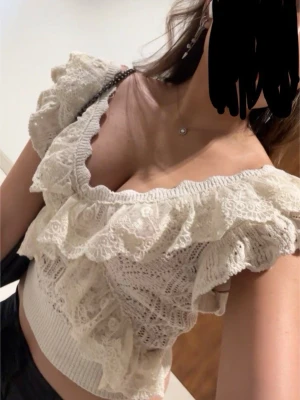 Vit spetsig topp från Zara - Säljs inte längre  - Supersöt vit topp med spets och volanger. Toppen är croppad och har bred resår i midjan samt djup v-ringning. Perfekt för dig som gillar romantiska detaljer och en feminin look.