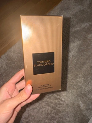 Tom Ford Black Orchid Eau de Parfum - Lyxig parfym från Tom Ford, Black Orchid, i en elegant guldig förpackning med räfflad yta och svart logotyp. Flaskan innehåller 50 ml Eau de Parfum och har en exklusiv och modern design som verkligen sticker ut.