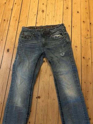 Rock Revival jeans - Säljer ett par blåa bootcut jeans från Rock Revival med slitningar och broderade detaljer på bakfickorna. 
