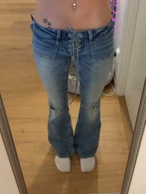 Blå lace-up jeans från Gina Tricot - Säljer ett par ljusblå jeans från Gina Tricot med snörning framtill och utsvängda ben. Jeansen har slitningar vid knäna och är tillverkade i klassisk denim. 