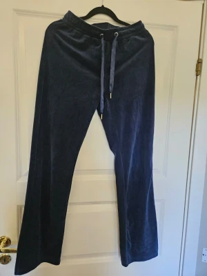 Marinblå velourbyxor Gina Tricot XS - Mörkblå mjukisbyxor i mjuk velour från Gina Tricot. Byxorna har raka ben, resår i midjan och dragsko med metalländar. Perfekta för chill dagar eller när du vill vara extra bekväm.