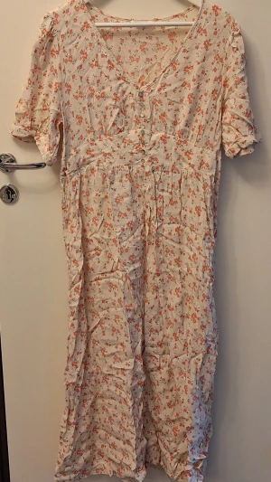 Blommig klänning från Indiska - Blommig klänning från Indiska. Klänningen har v-ringning, knappar framtill och korta puffärmar.