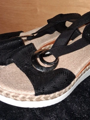 Sandaler  - Sandaler med svart ormmönstrad ovandel och elastiska band. Dekorativa metallringar framtill och flätad beige sula ger en trendig look. Vit platåsula för extra höjd och komfort. 