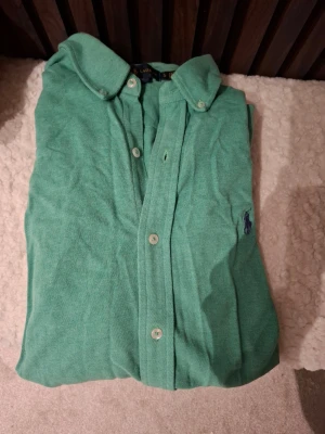 Grön skjorta från Ralph Lauren - Snygg grön skjorta från Ralph Lauren med klassisk krage och knäppning framtill. Skjortan har broderad logga på bröstet och är tillverkad i bomull. Perfekt för en stilren look.