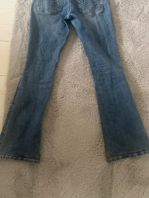 Bootcut jeans med fickdetaljer - Säljer ett par klassiska blå bootcut jeans med snygga fickdetaljer bak. Jeansen har utsvängda ben och normal midja, perfekta för en avslappnad och trendig look. Säljer då dem inte kommer till användning! använda men fint skick storlek 38 men passar även S