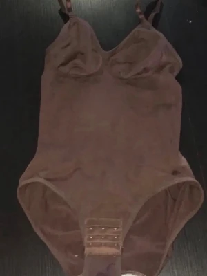 Brun body med justerbara axelband - Bruk body med justerbara axelband i storlek S. Den är gjort av 85% Polyamid och 15% elastan vilket gör den både bekväm, drar in midjan och ger ett ”snatched” resultat.