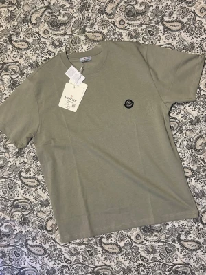 Moncler T-shirt, helt ny.  - T-shirt med moncler logo på bröstet. Emblem metall. Färg grå. 