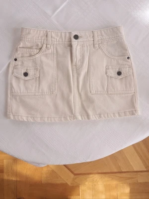 beige minikjol med fickor - super snygg ljusbeige minikjol med fickor och knappdetaljer framtill 💕 säljer pga att den aldrig kommer till användning (använd 2 gånger) kjolen är ca 37 cm tvärs över midjan och ca 32 cm lång! 