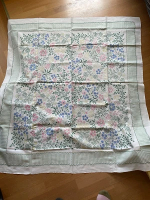 Vintage Blommig duk i pastellfärger - Säljer en vintage film med blommigt mönster i pastellrosa, blått och grönt på vit botten. Sjalen har en bred, ljusgrön rand runt kanten och är perfekt att ha på sommarbordet . Materialet är vad som användes förr nån linne kvalité 
