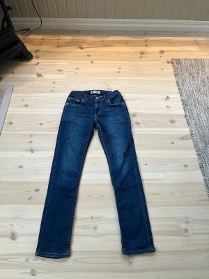Mörkblå raka jeans från Levi's - Snygga mörkblå jeans från Levi's med klassisk femficksdesign och raka ben. Jeansen har en stilren look med kontrastsömmar och läderpatch bak i midjan. Perfekta för en avslappnad och trendig stil.