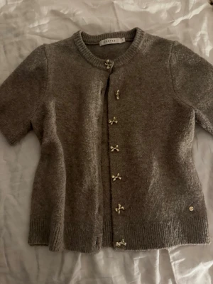 Brun kofta med rosettknappar från Costes - Kortärmad ljusbrun kofta från Costes med söta rosettformade knappar framtill. Väldigt söt och unik pga rosettknapparna 💕