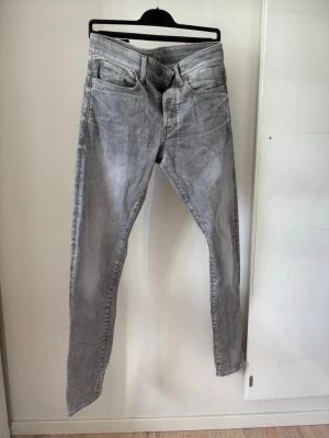 G star 3301 Tapered - Säljer ett par ljusgrå slim fit jeans med klassisk femficksmodell och dragkedjegylf. Jeansen har en tvättad look och raka ben. Perfekta för dig som gillar en stilren och avslappnad vibe.